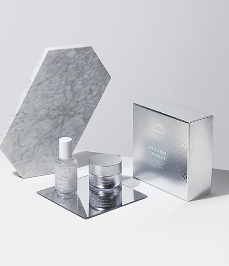 Caviar infused skincare set positioned on a mirrored surface against a silver background.