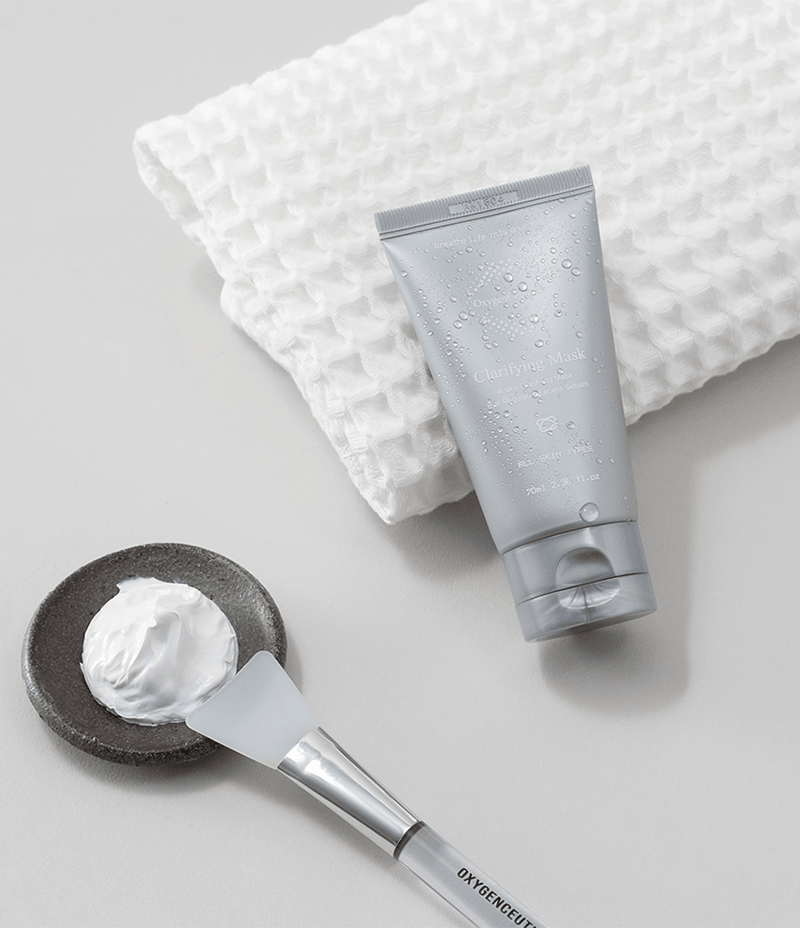 Towel holding a tube of acne relief Clarifying Mask with fresh water droplets on it.