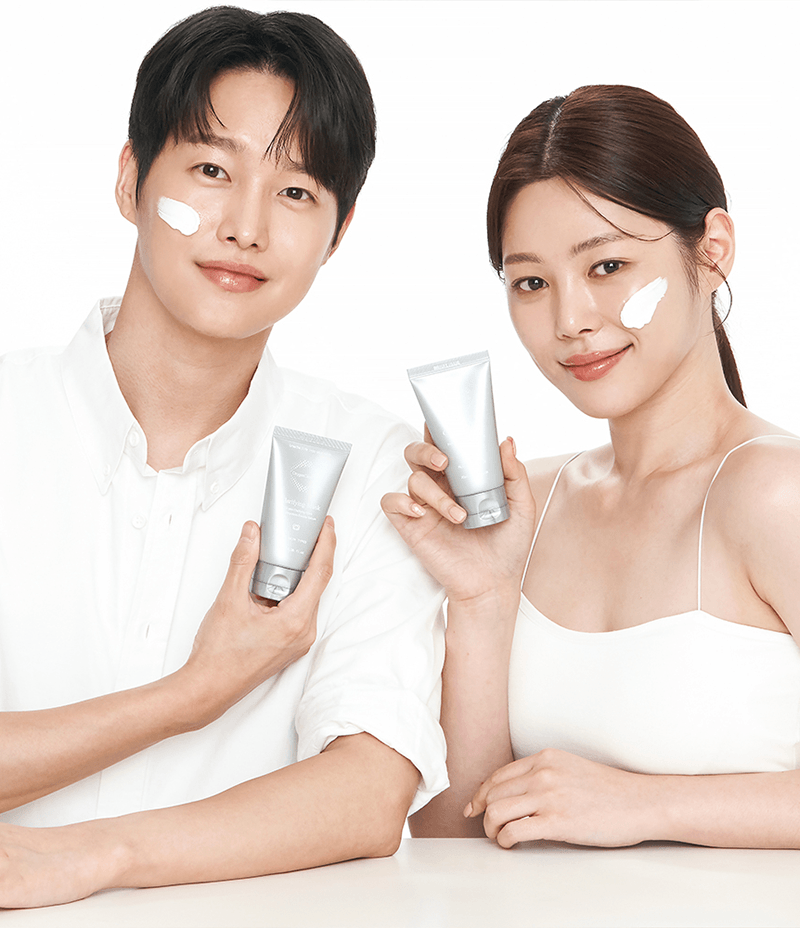 Two Korean models showcasing a tube of brightening Clarifying Mask, demonstrating its application on their cheeks.
