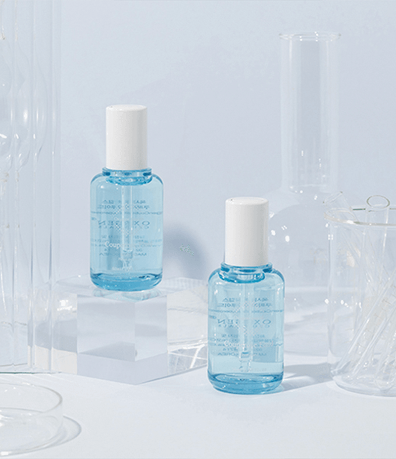 Two travel-friendly bottles of Couperose Fluid for couperose skin placed on a pastel blue surface, complemented by laboratory tools and beakers for skin research.