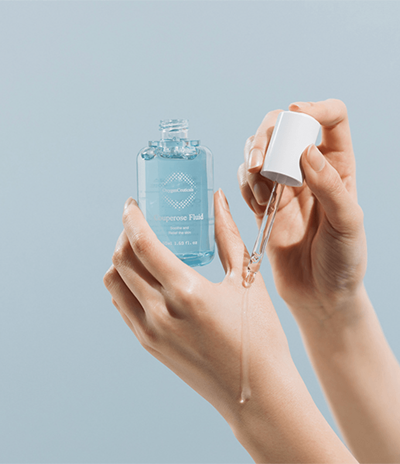 Use of Couperose Fluid for rosaeca skin condition, demonstrated on hand with a serene, pale blue background.