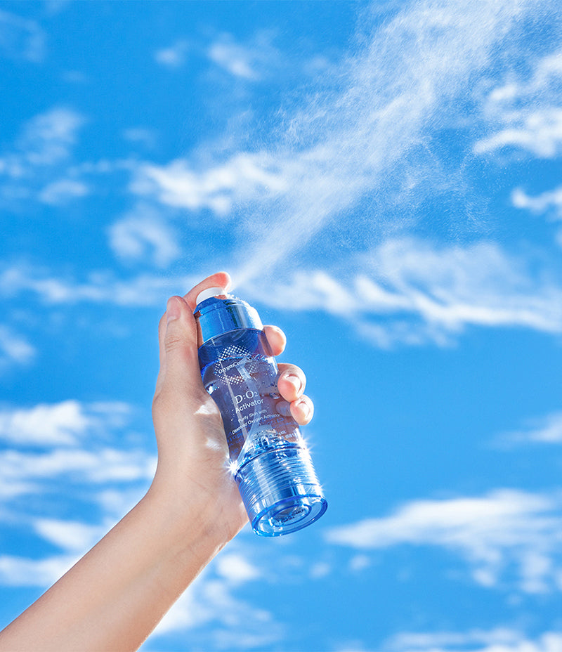 A person holding a D:O2 Activator spray bottle, spraying water against a backdrop of a clear blue sky.