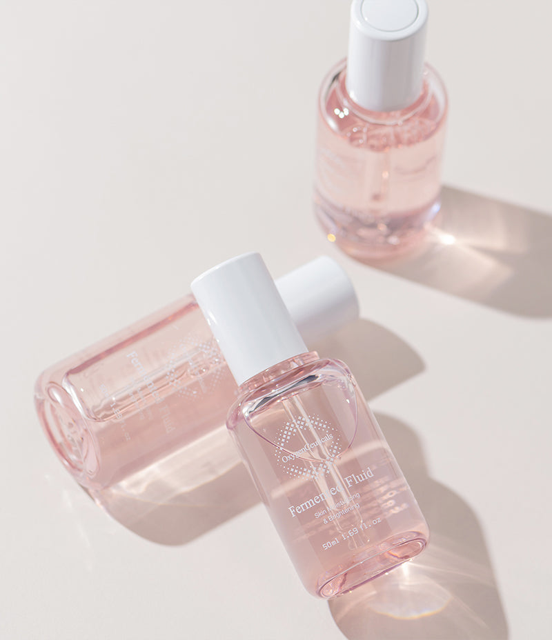 Brightening serum in form of pink Fermented Fluid in three elegant bottles on a pale pink background.