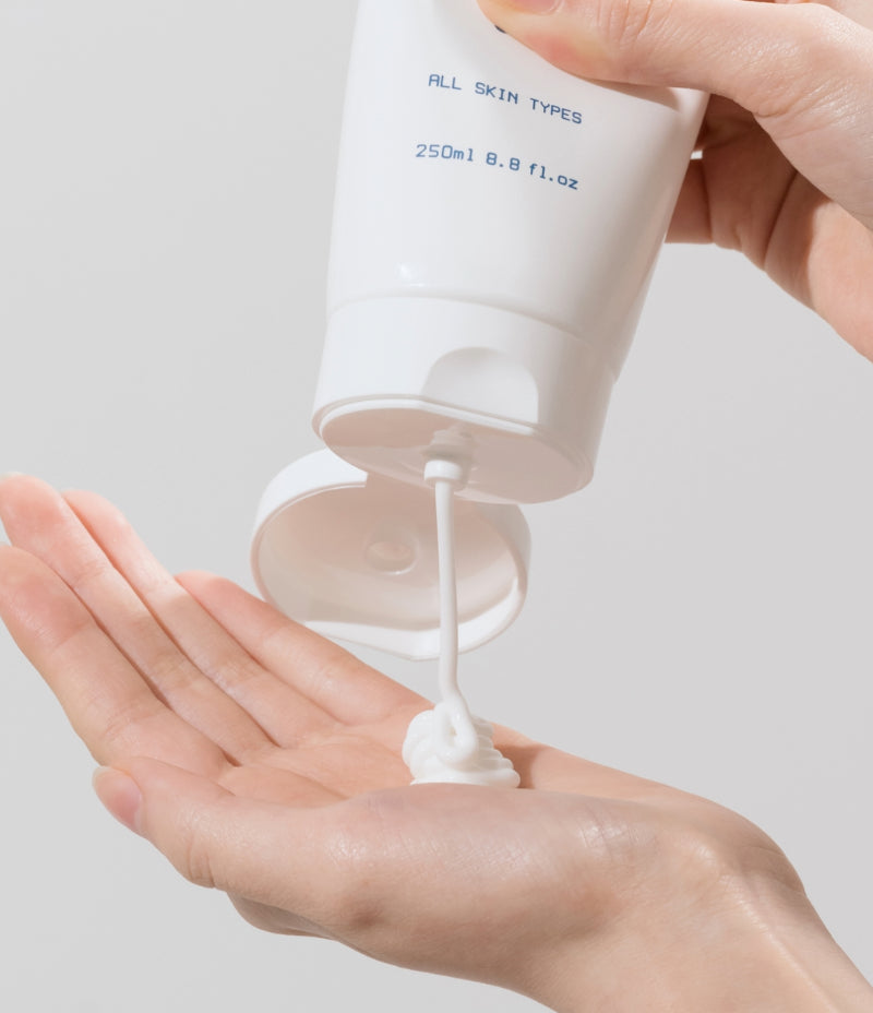 Person squeezing Gentle Facial Cleansing Lotion onto hand to display milky soft texture.
