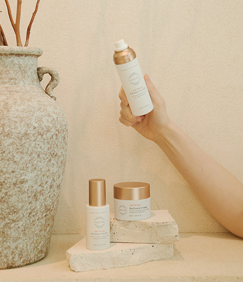 A hand showcasing the ReGenon Activator to combat aging skin, with other parts of the ReGenon set neatly arranged on a stone backdrop.