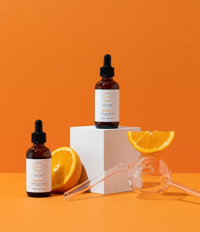 An orange placed on a table, alongside a serum labeled "Serum 12/17" for antioxidant and brightening care.