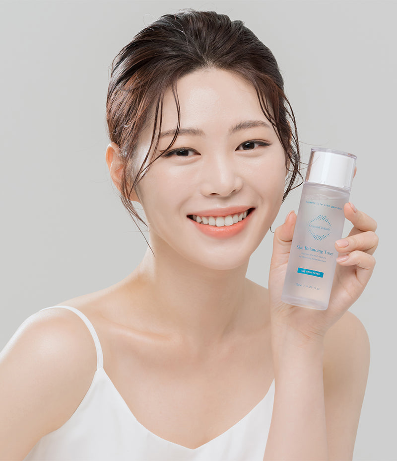 A female holding up a bottle of Skin Balancing Toner, a CICA-based solution for maintaining skin's pH balance and for toning of skin.