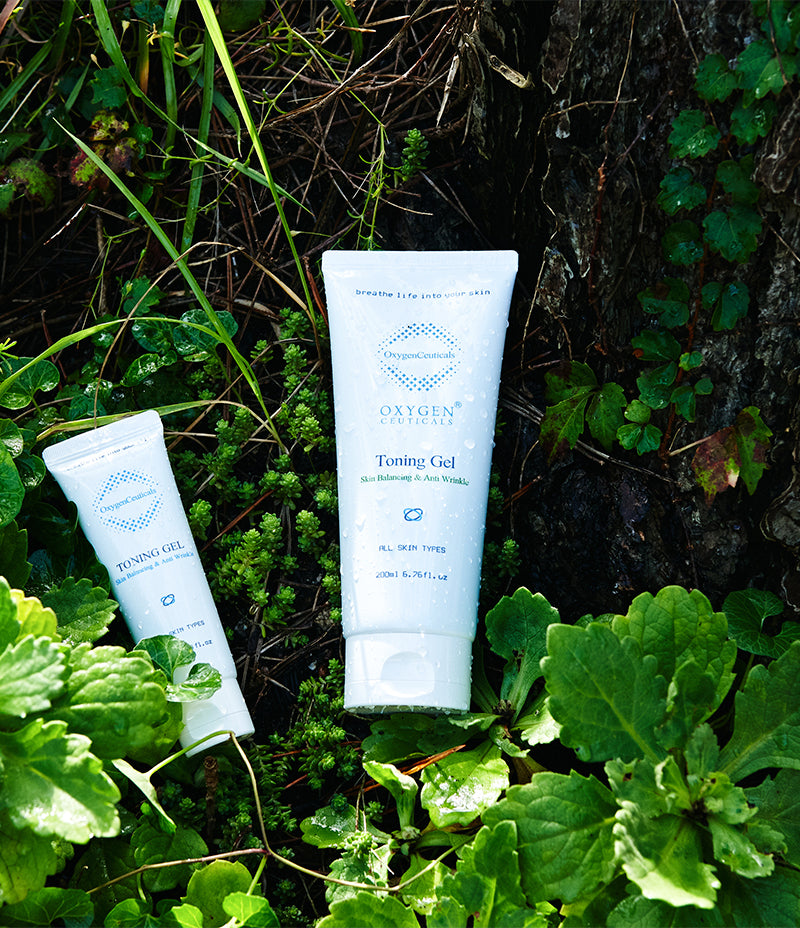 A tube of gel toner and another tube lying on the a pile of greenery, both labeled as 'Toning Gel'. For toning of skin.  Sensitive skin. Helps acne. Includes cica, centella leaf extract. Oxygen gel. 