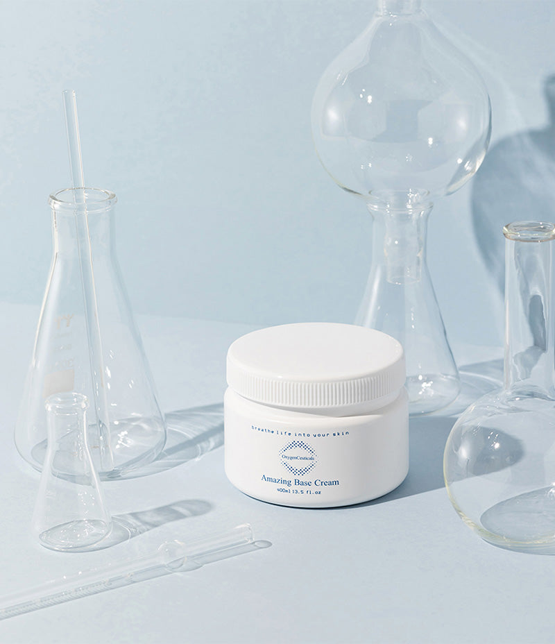 The Amazing Base Cream tub, formulated for ultra dry skin, positioned with laboratory glassware on a soft blue backdrop.