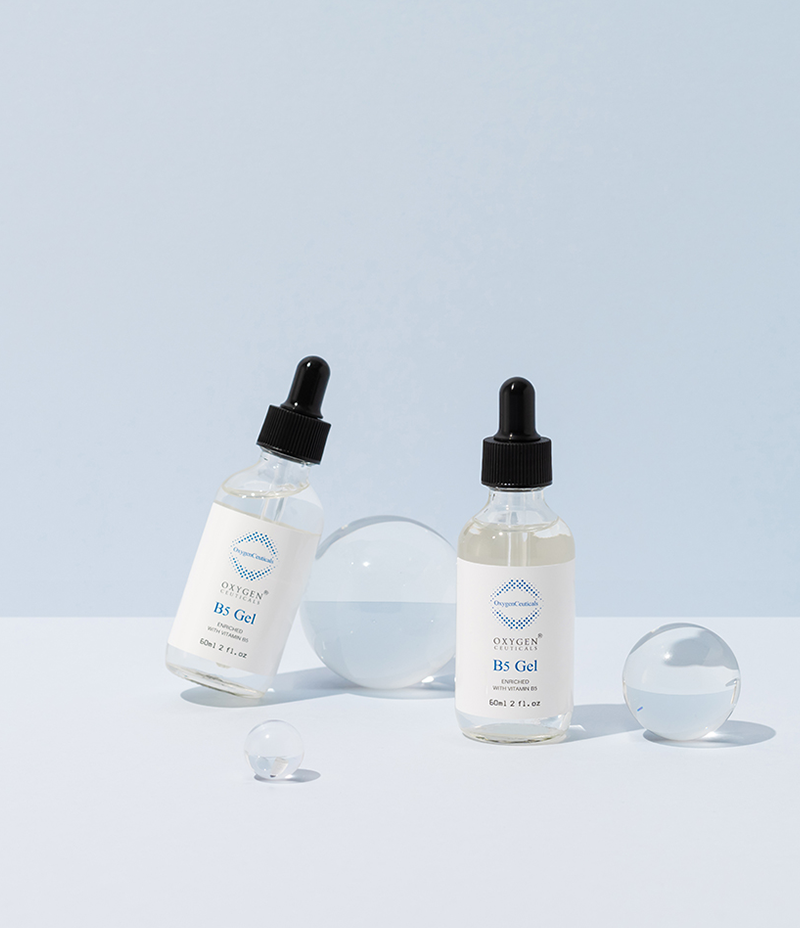 Two bottles of B5 Gel stand in front of a pastel blue background next to clear glass spheres. 