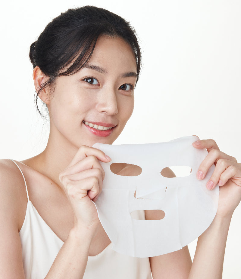 Woman enthusiastically presenting a CC Mask used for redness relief with a bright smile. 