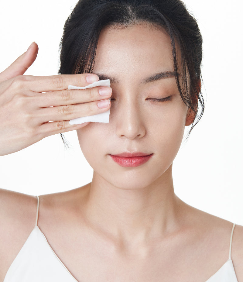 An image of a woman holding a cotton pad over her eyes, using OxygenCeuticals Double Makeup Remover for effective cleansing and makeup removal.