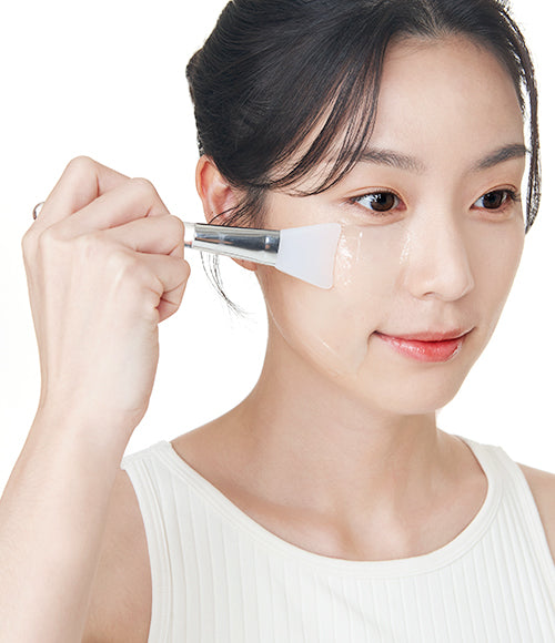 A woman spreading HA Gel on her face with a silicone brush, prepping for oxygen face mask treatment, showcasing the thick and rich texture of the gel. 