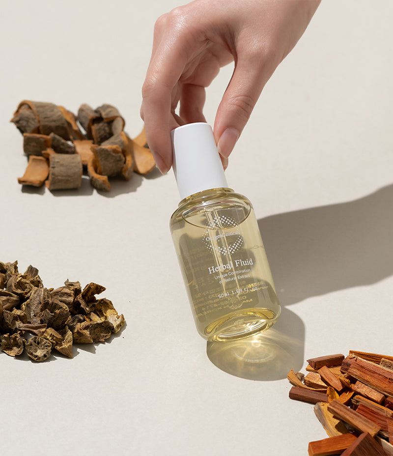 A hand presenting a bottle of herbal complex mixture, with a natural selection of herbs and bark in the background.
