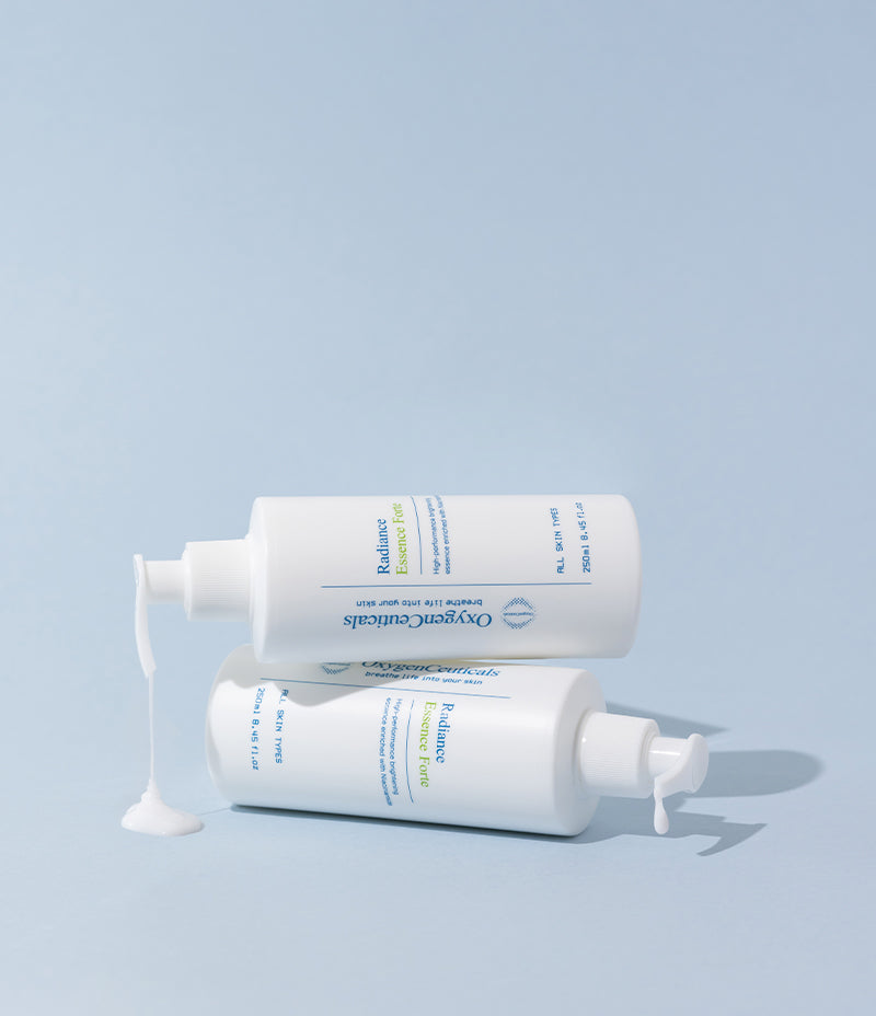 Image showcasing two bottles of brightening essence Korean skincare product, Radiance Essence Forte, artfully stacked and leaking lotion, set against a pastel blue setting.