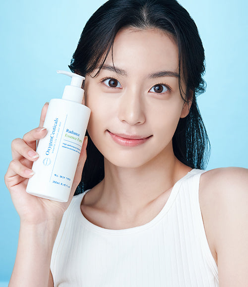 Enthusiastic woman showcasing a bottle of Kbeauty essence known as Radiance Essence Forte against her smiling face.