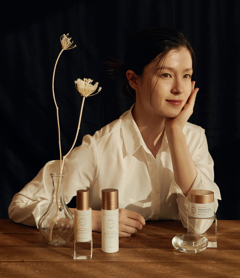  woman elegantly posing behind an assortment of anti-aging skincare routine products from the ReGenon Rewind Kit.