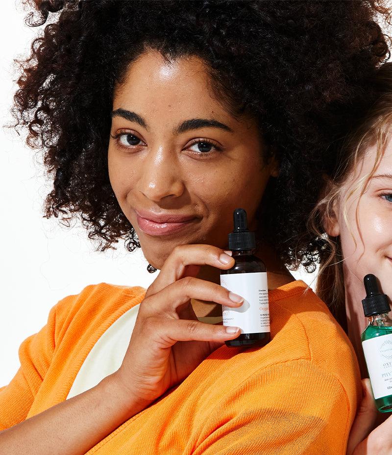 Two women showcasing skin care products, including Serum 12/17 with Vitamin C and E for brightening and antioxidant benefits.