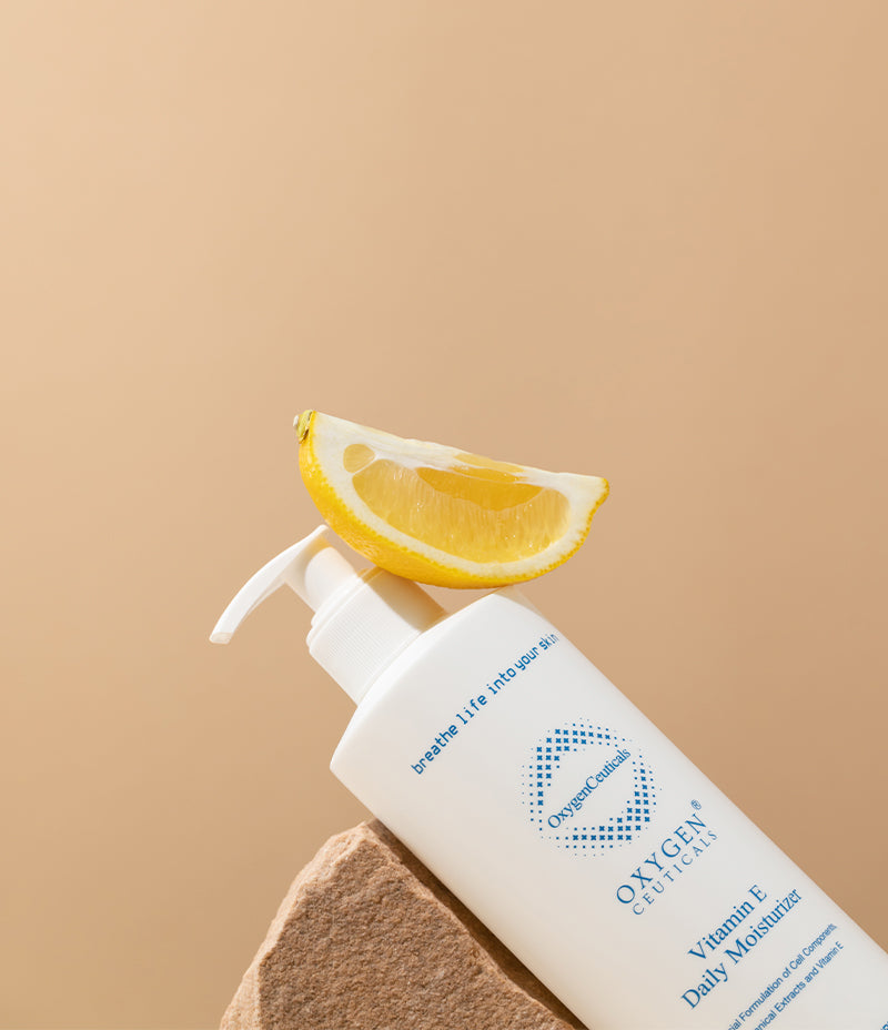 A bottle of Vitamin E daily moisturizer with antioxidant power, accompanied by a slice of grapefruit.